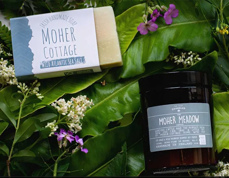 Moher cottage own brand candle and soap on bed of flowers and leaves