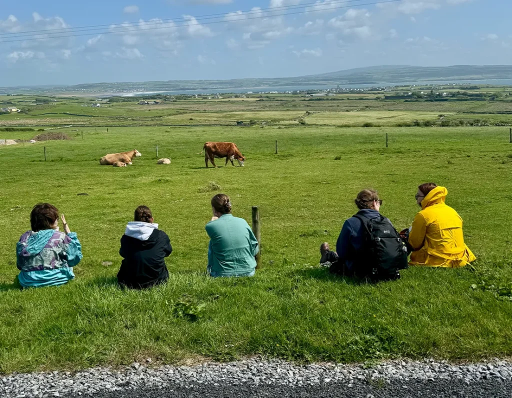 Group sit in grass with cow in front of them