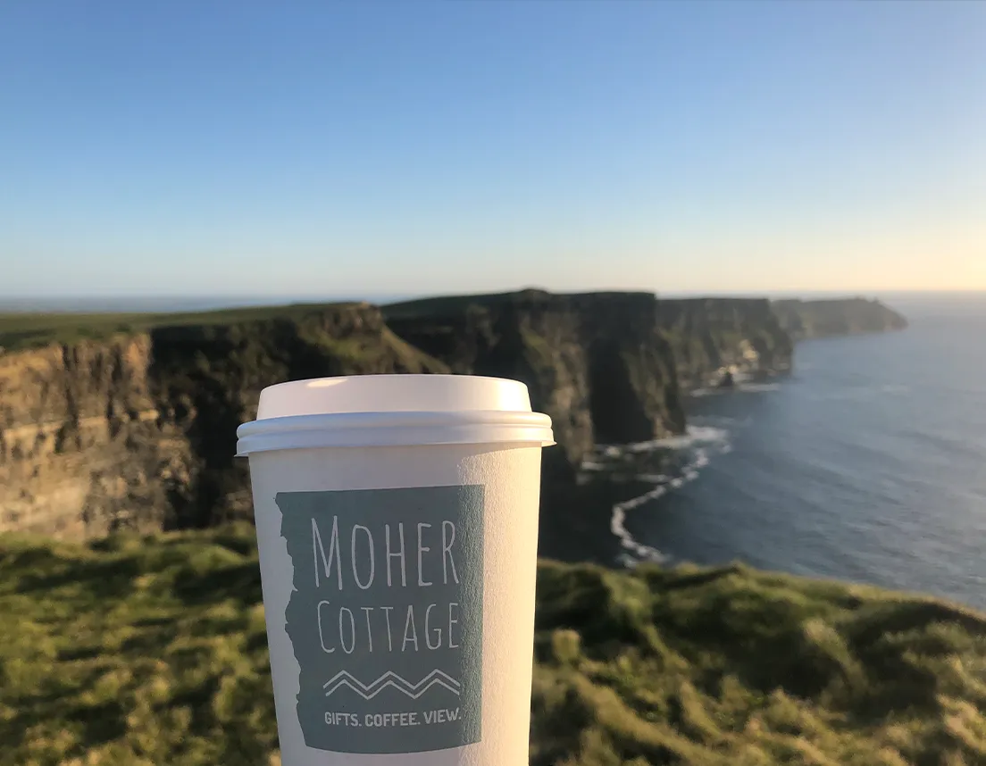 Moher cottage coffee cup being held in front of cliffs