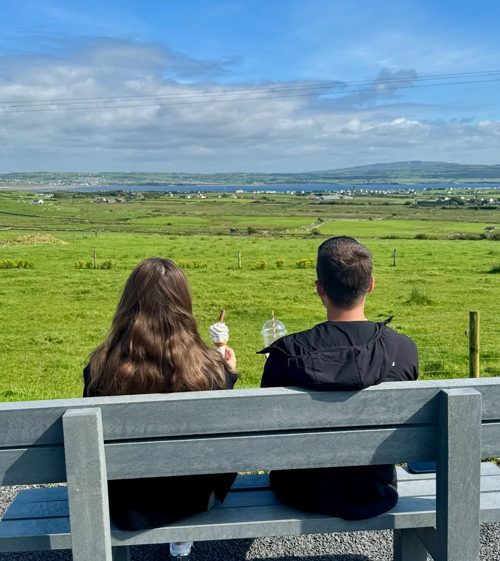Man and Woman sitting on bench with ice cream and coffee admiring view