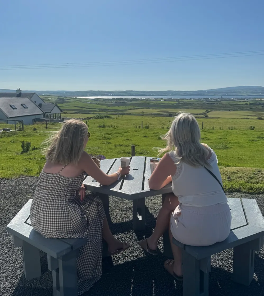 Two women enjoing sun sitting at table overlooking view